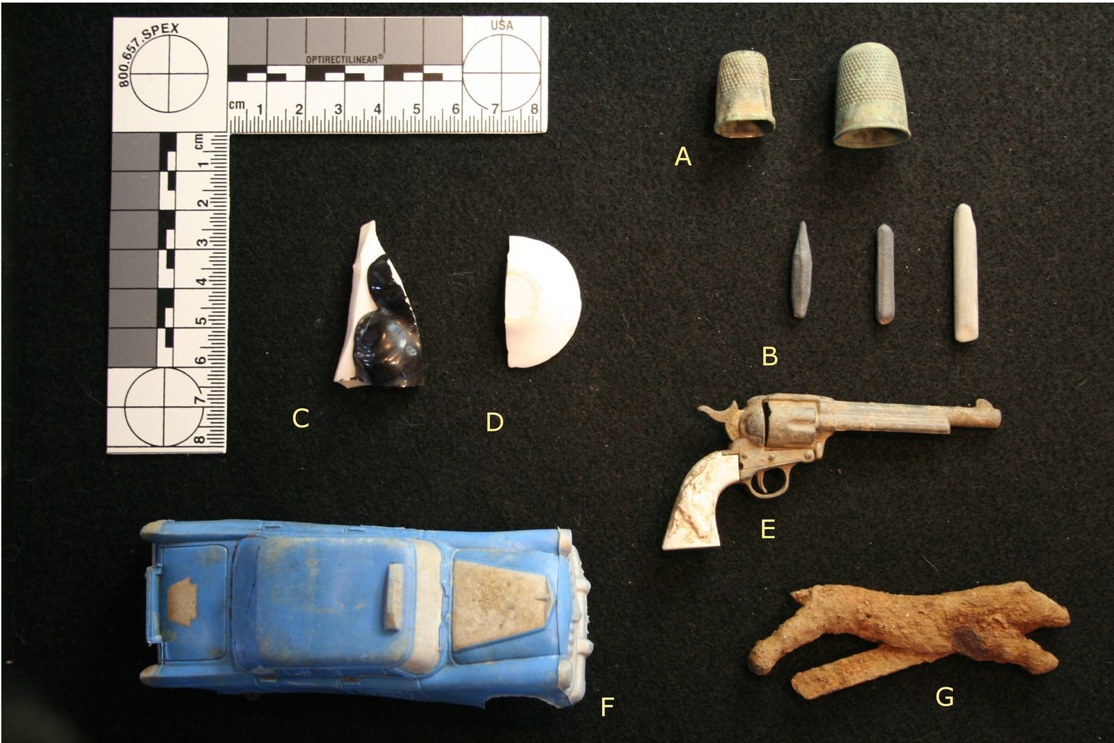 Historic artifacts including a toy pistol, a toy car and porcelain doll parts laid out with a photo scale